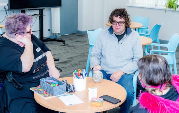 A group of three people are sitting round a table chatting.