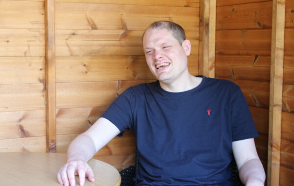 One of Southdown's learning disability clients is sat laughing in their wooden summer house.