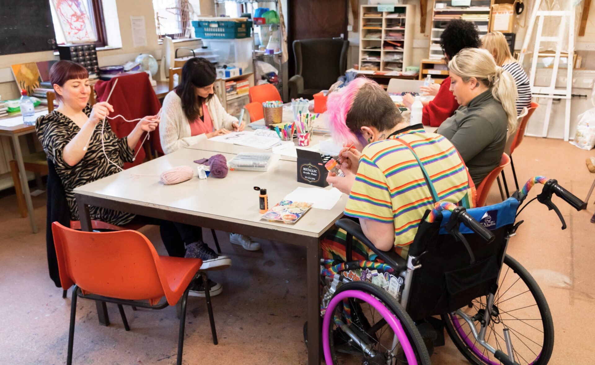 A group of people are sat around a table doing art work.