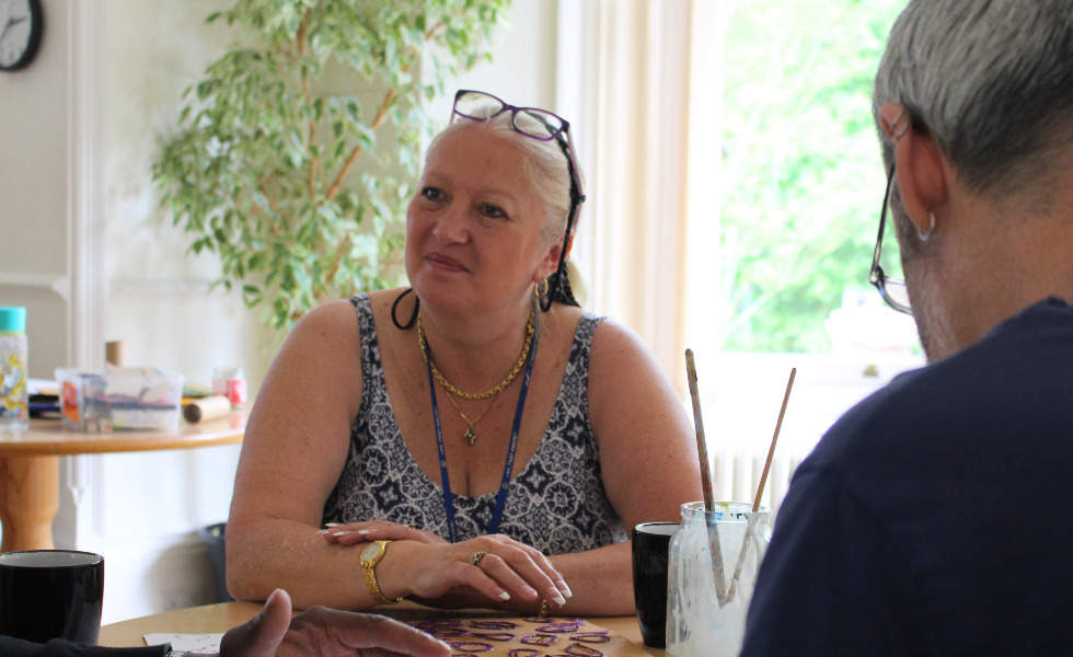 Southdown client is in a craft workshop. They are smiling and looking across to somebody on the table with them.