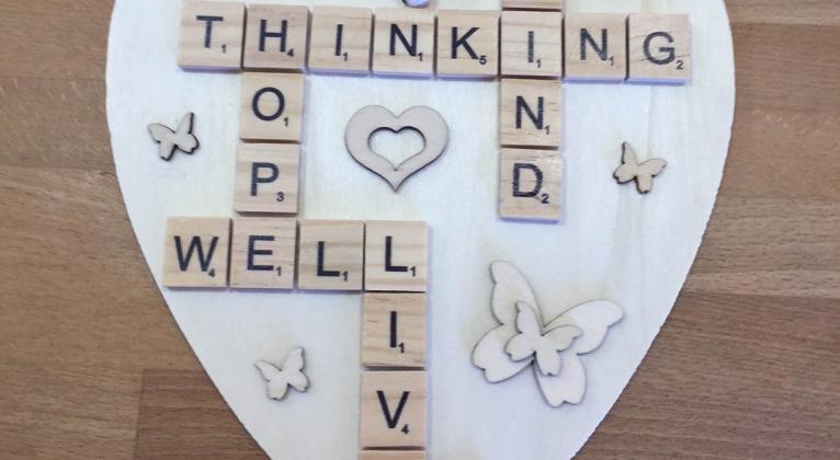 Close up photo of a wooden heart with scrabble letters including Thinking Well