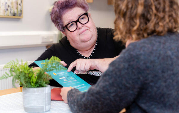 Photo of mental health worker and client sat at table holding a visual document