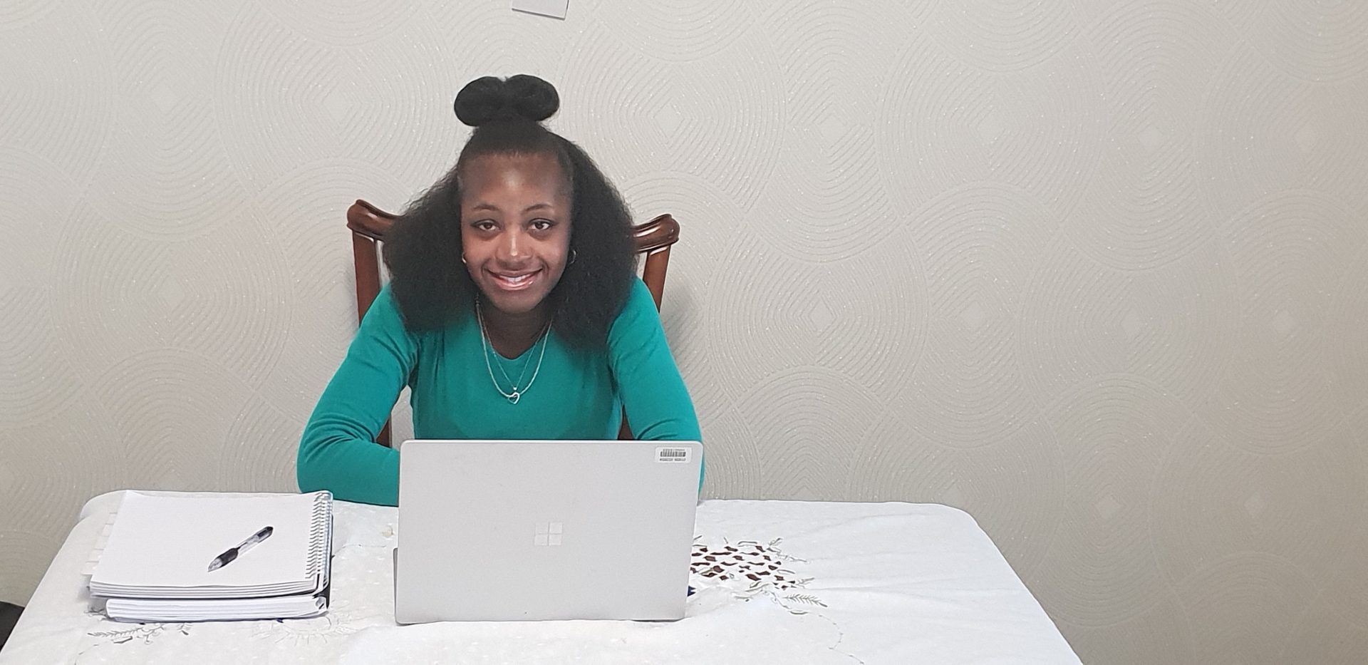 A black woman wearing a green top sits at her laptop smiling at the camera