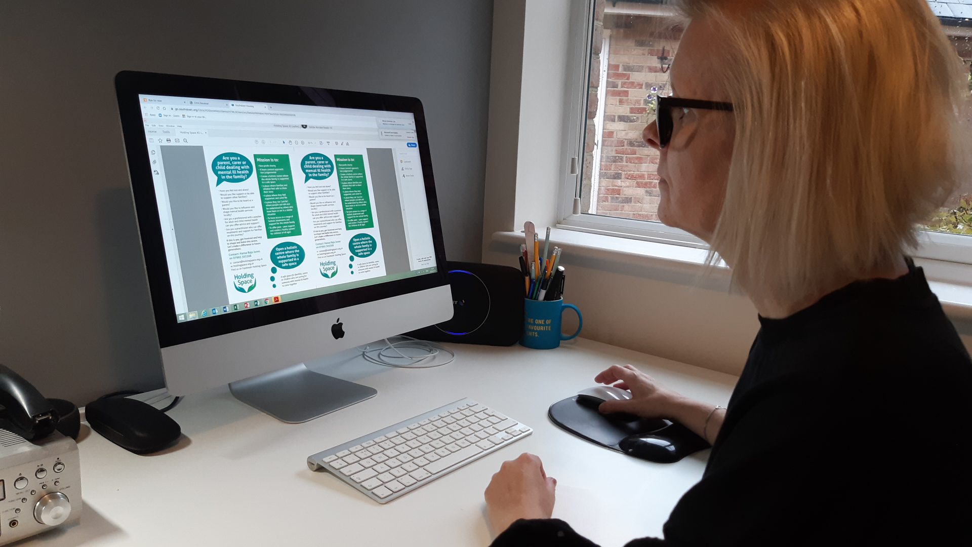 A woman with short hair wearing glasses looks at her desktop computer