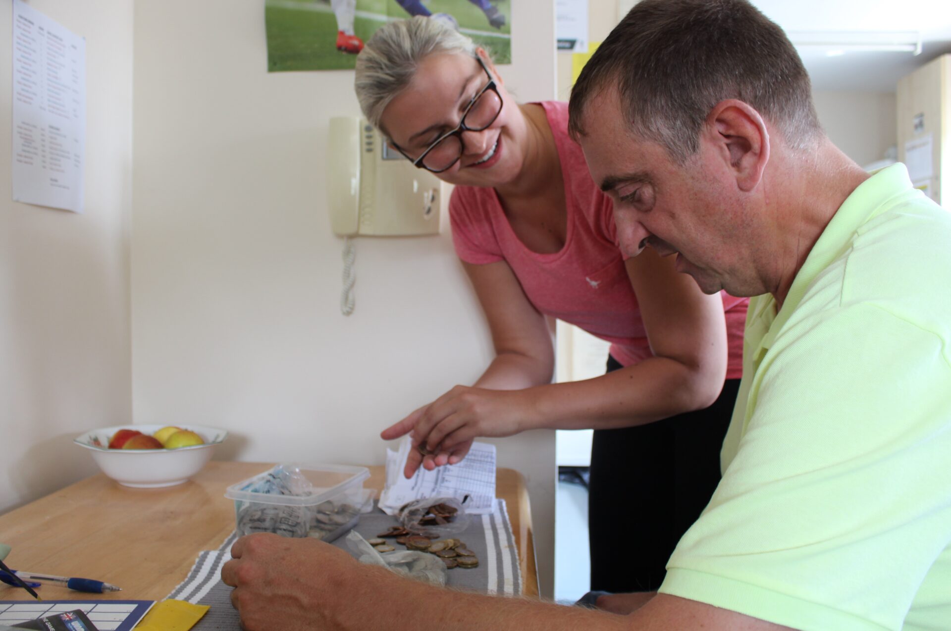 A woman with blonde hair and glasses helps a man with casual shirt on count money