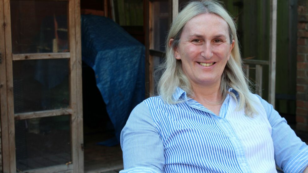 A woman with blonde hair sits outside smiling at camera