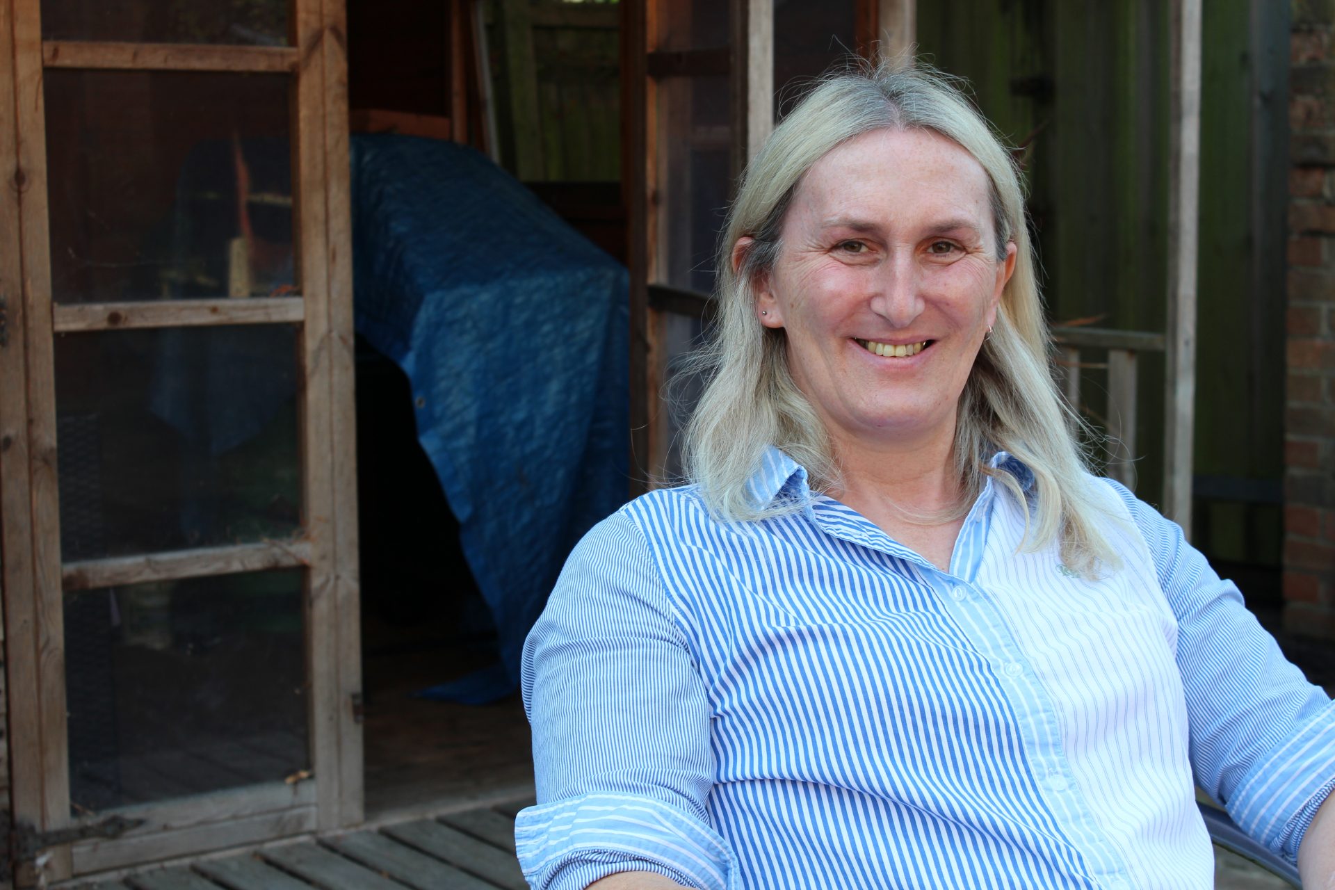 A woman with blonde hair sits outside smiling at camera