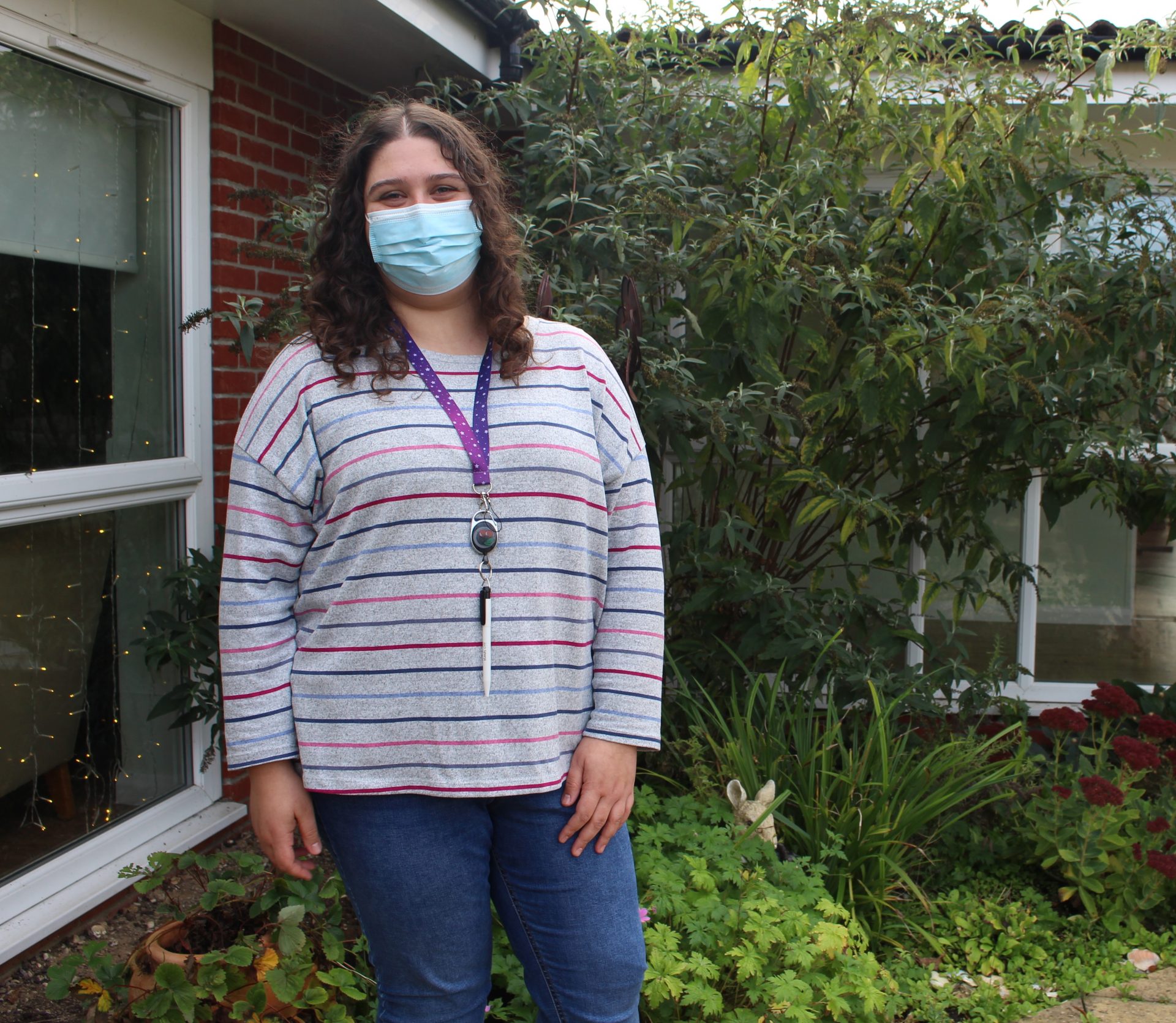 A Learning Disability Support Worker stands in garden wearing a mask and stripey top