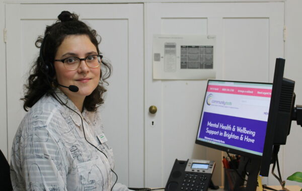 worker with brown wavy hair sits at computer with headset on