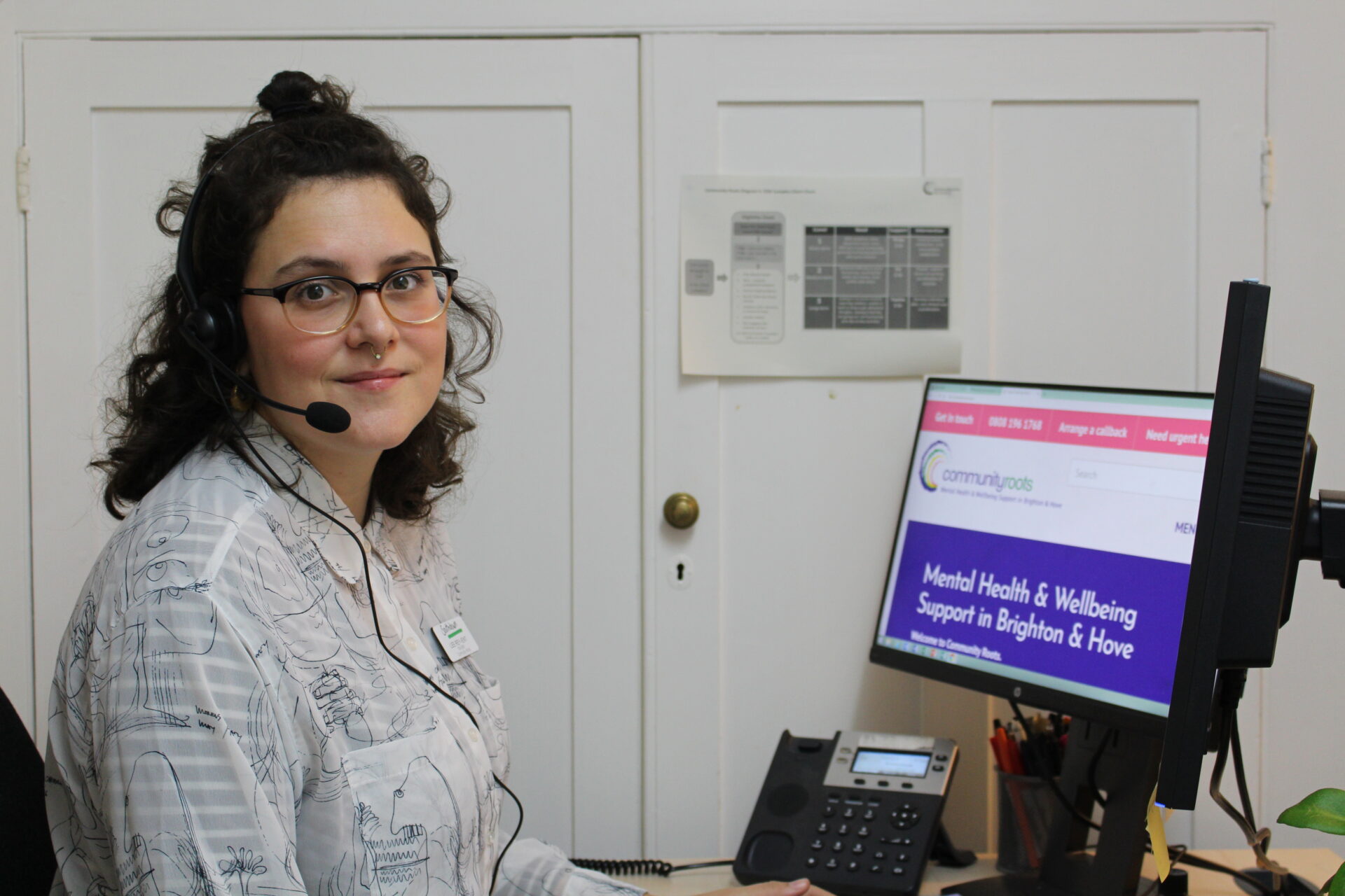 worker with brown wavy hair sits at computer with headset on