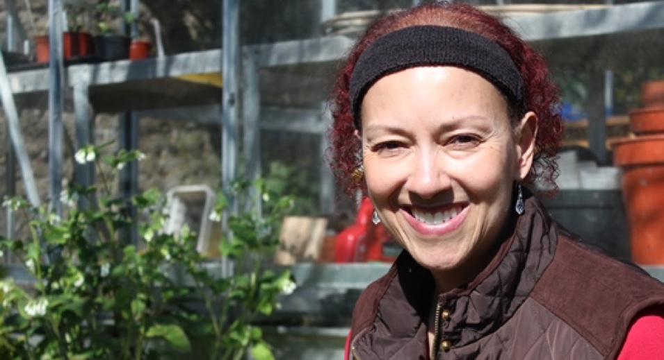 A woman with red curly hair sits in front of a greenhouse