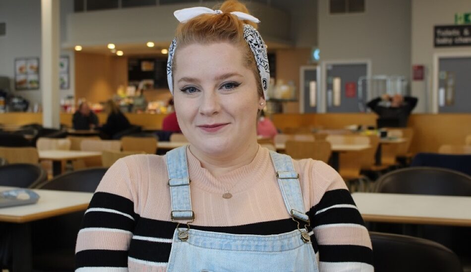 Close up photo of person smiling, wearing casual clothes with cafe seating in the background