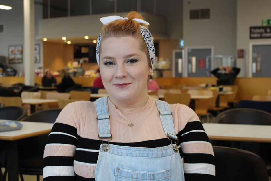 Close up photo of person smiling, wearing casual clothes with cafe seating in the background