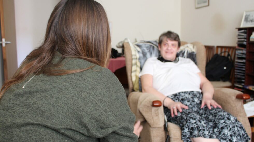 a worker with long hair sits looking at a tenant who is in her armchair