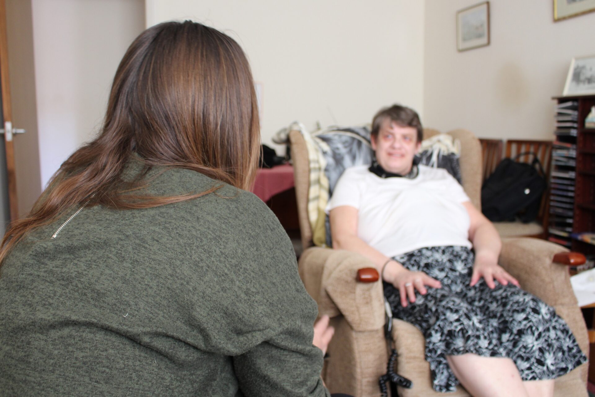 a worker with long hair sits looking at a tenant who is in her armchair