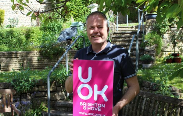 Photo of UOK Team member stood holding board showing new bright pink UOK logo and web address
