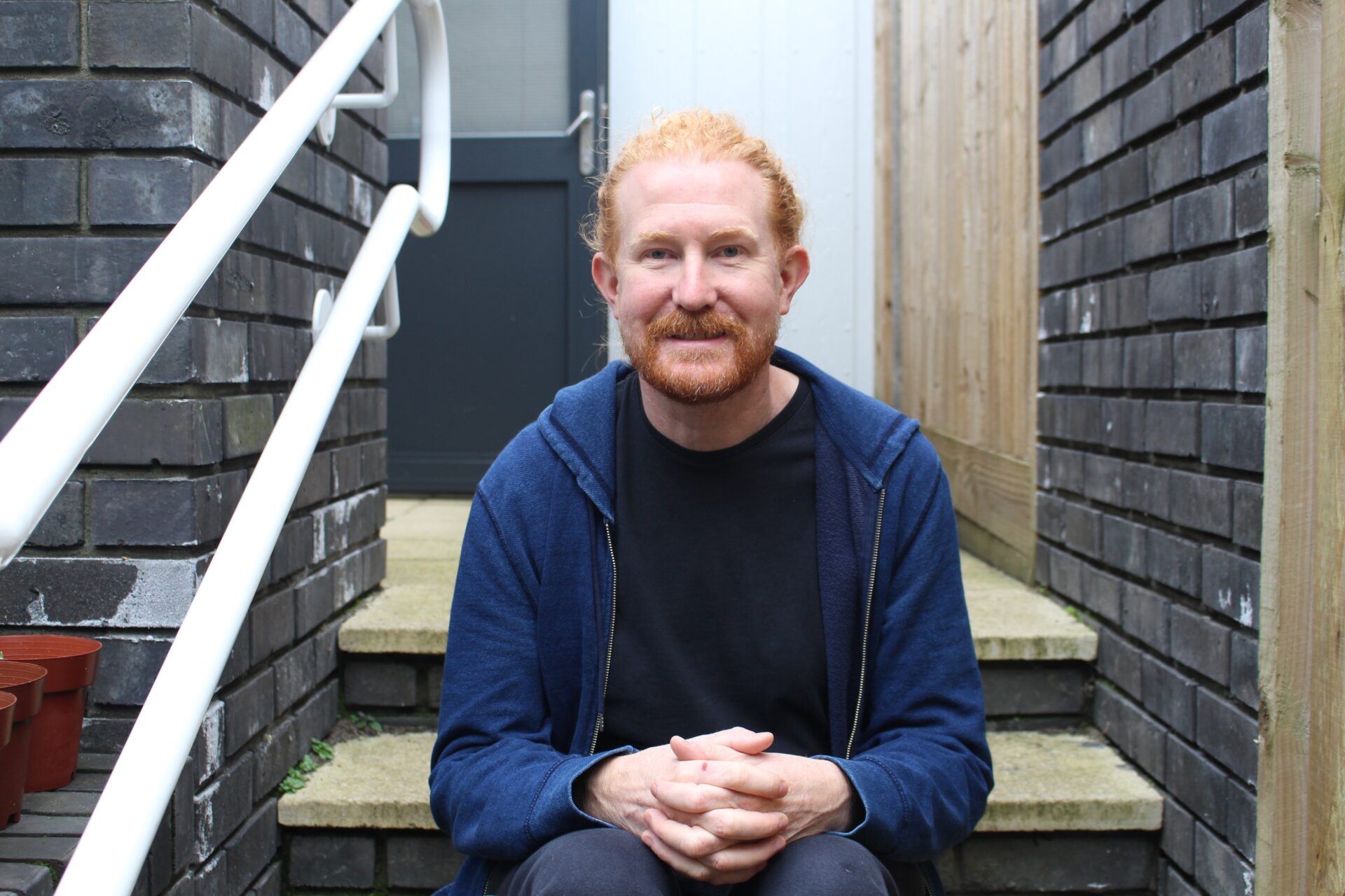 A man with red hair and beard sits on the steps of a learning disability support service