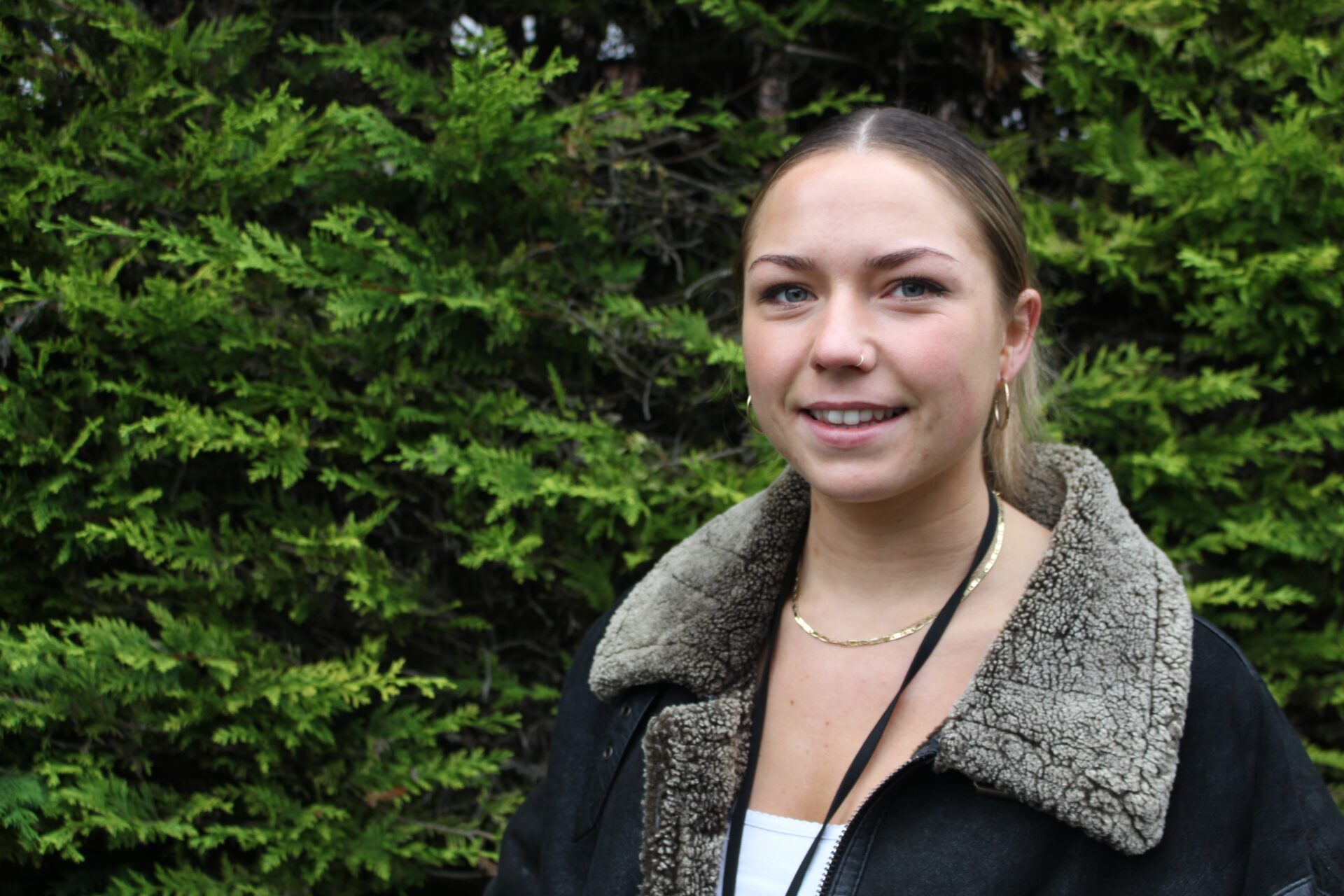 A young woman with hair tied back smiles at the camera