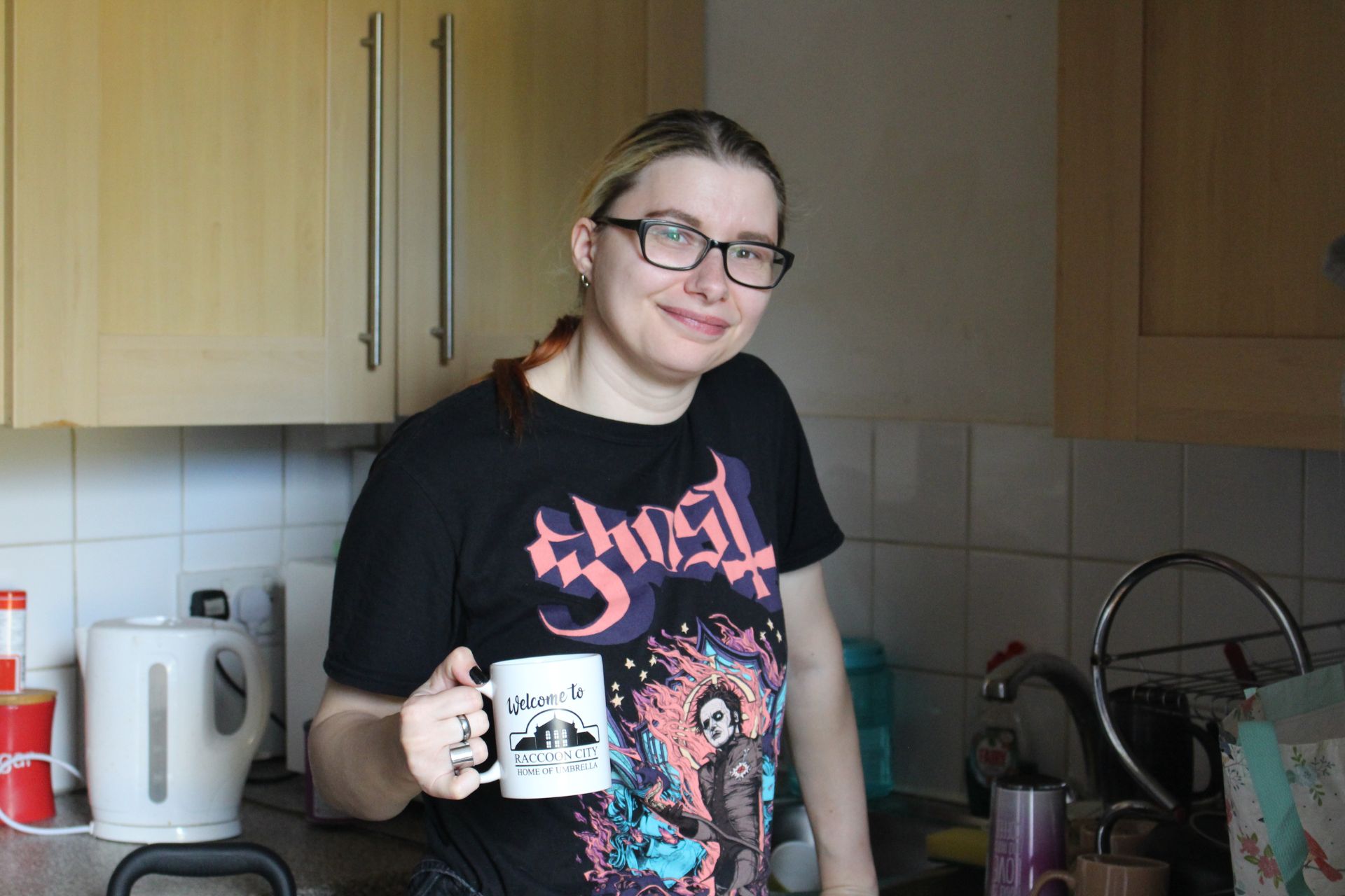 Photo of person standing and smiling in kitchen holding a mug