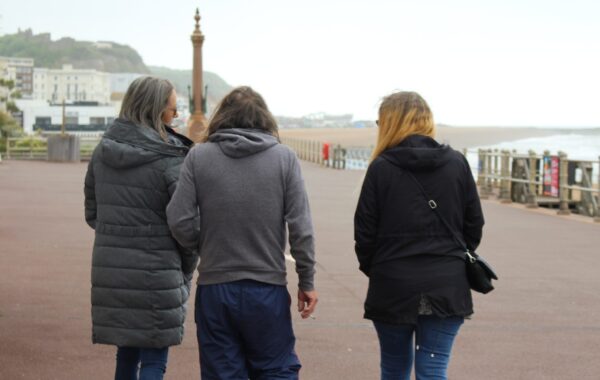 Three outreach workers walking alongside a person they support on a seaside promenade, symbolising guidance and housing support for people at risk of homelessness.
