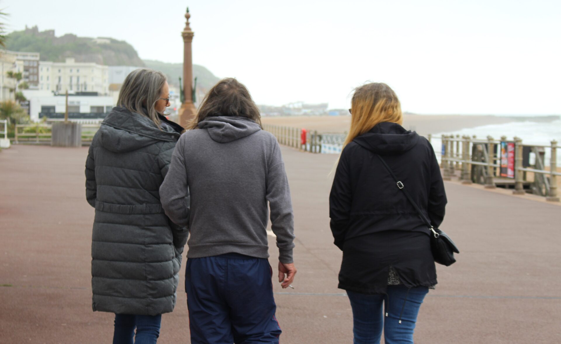 Three outreach workers walking alongside a person they support on a seaside promenade, symbolising guidance and housing support for people at risk of homelessness.