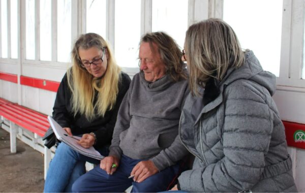 Photo of client sitting in bus shelter side by side between two workers, looking at a form together