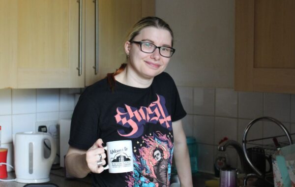 Photo of person standing and smiling in kitchen holding a mug