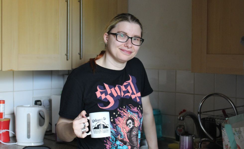 Photo of person standing and smiling in kitchen holding a mug