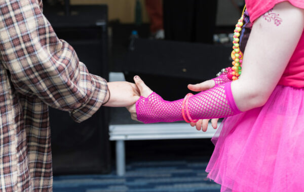 A man wearing a checked shirt holds hands of a woman dressed in a bright pink dress