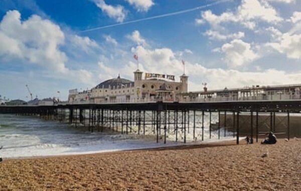 An image of Brighton Palace Pier with blue skies and big white clouds in the background, and pebble beach in the foreground.