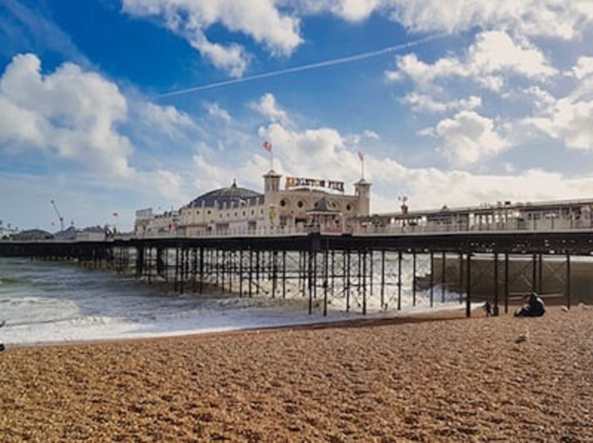 An image of Brighton Palace Pier with blue skies and big white clouds in the background, and pebble beach in the foreground.