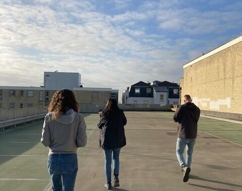 Three people are on the top floor of a multi-storey car park. The sky is blue.