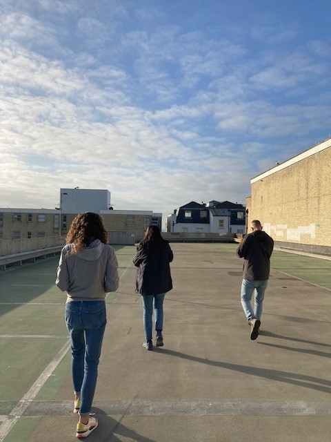 Three people are on the top floor of a multi-storey car park. The sky is blue.