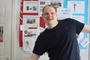 A client wearing a black t-shirt stands in front of his My Plan board with a smile on his face.