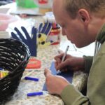 A white man with fair hair, wearing a green hoodie, is creating artwork