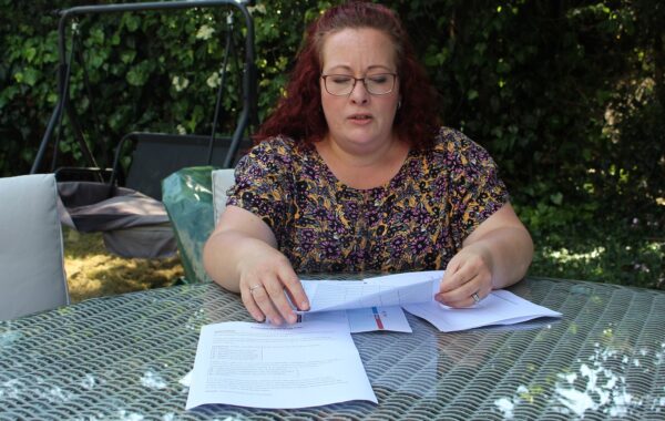 A woman with auburn hair, wearing glasses, is sitting at a garden table, looking at papers