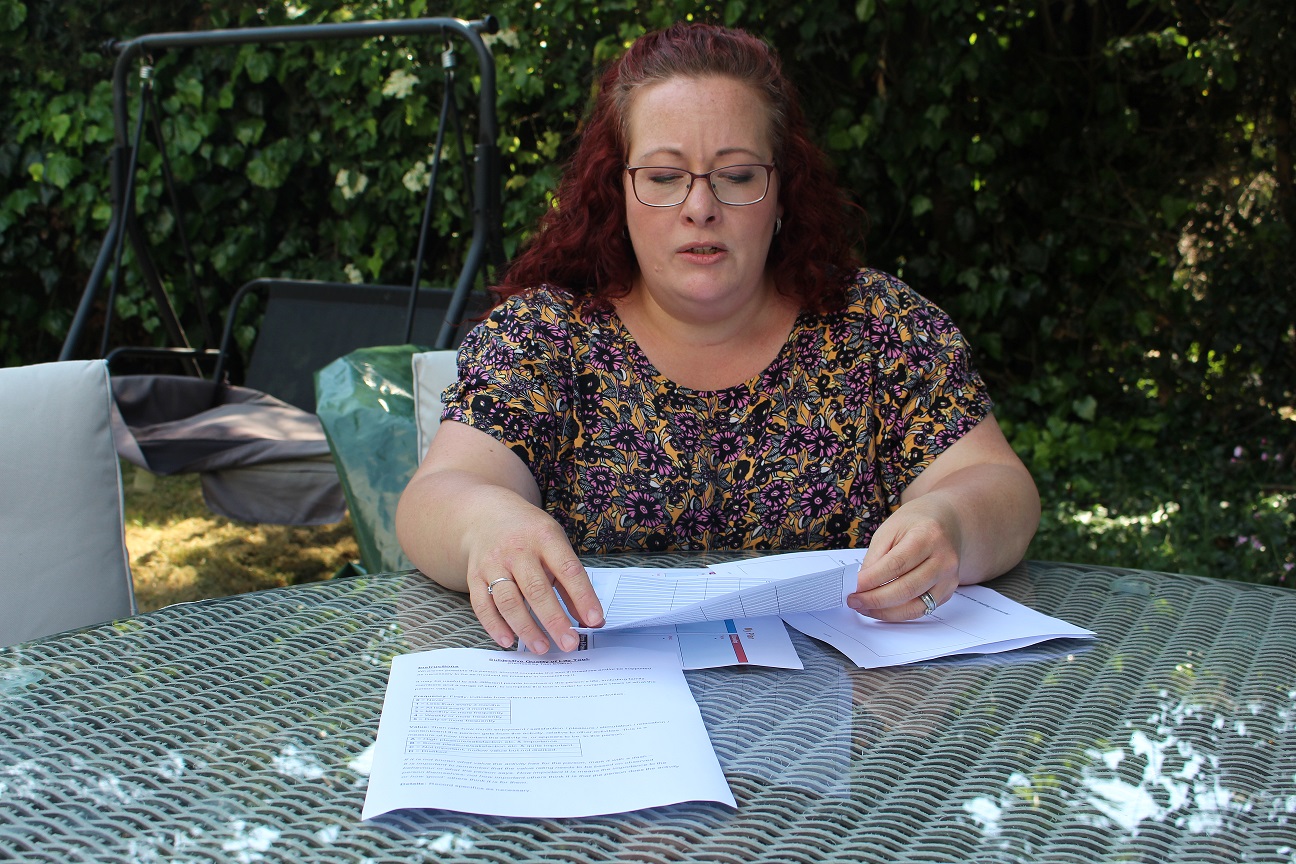A woman with auburn hair, wearing glasses, is sitting at a garden table, looking at papers