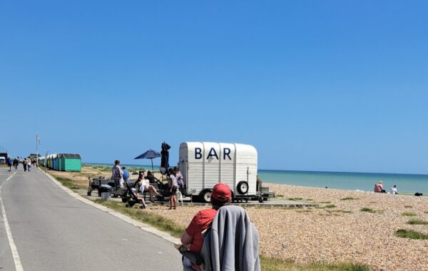 A man wearing a red t-shirt and cap heads towards a cafe bar on the beach in his wheelchair