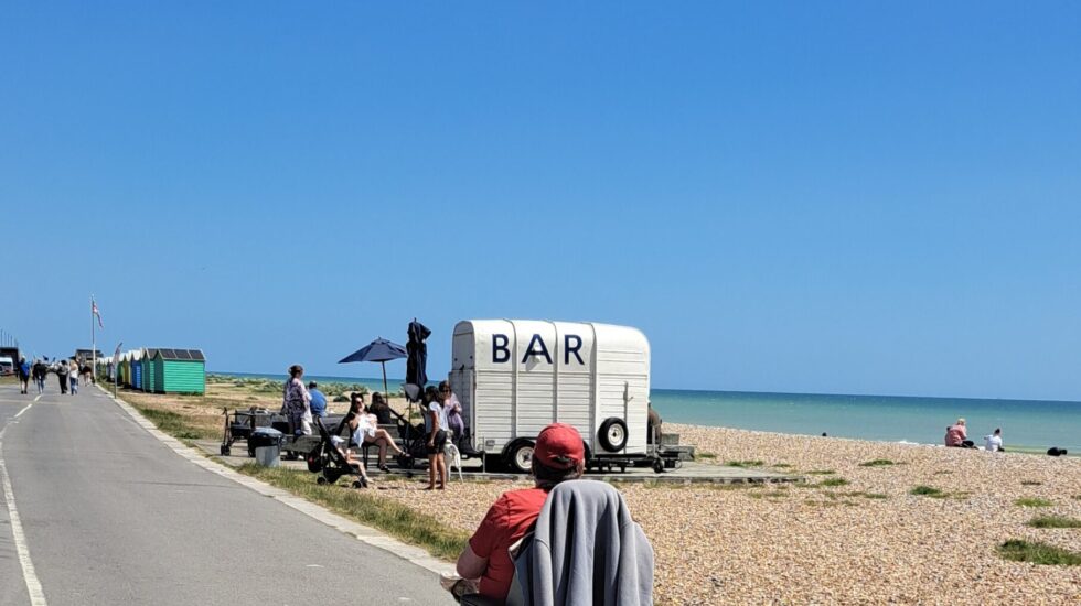 A man wearing a red t-shirt and cap heads towards a cafe bar on the beach in his wheelchair