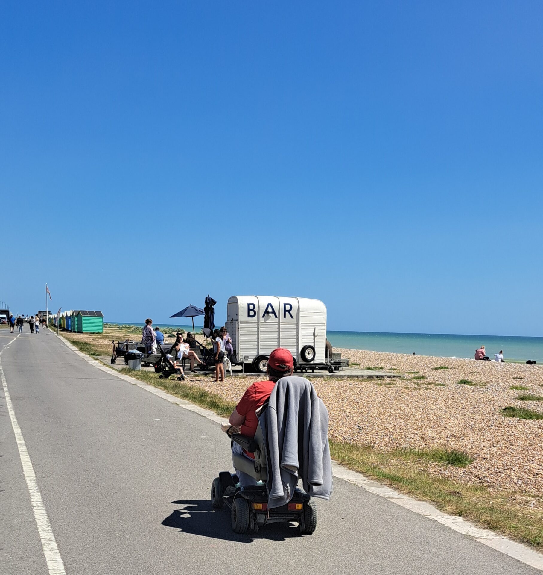 A man wearing a red t-shirt and cap heads towards a cafe bar on the beach in his wheelchair