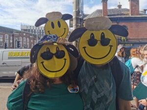 Three people are in a street wearing smiley face shaun the sheep masks