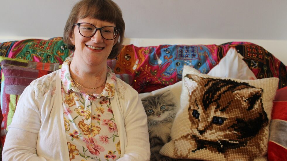 A tenant with disabilities sits in her living room smiling at the camera.