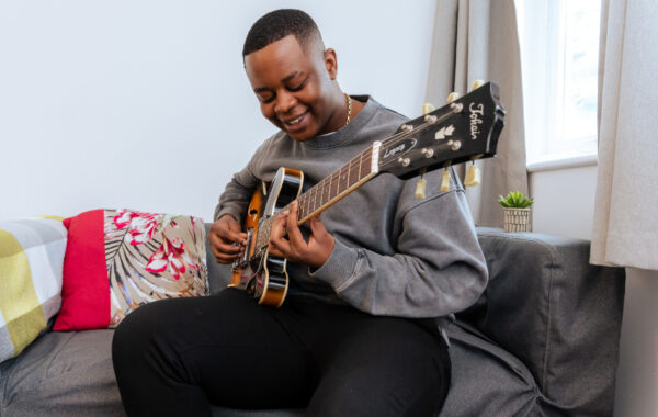 Southdown client is smiling whilst playing the guitar. They are sat on a sofa near the window.