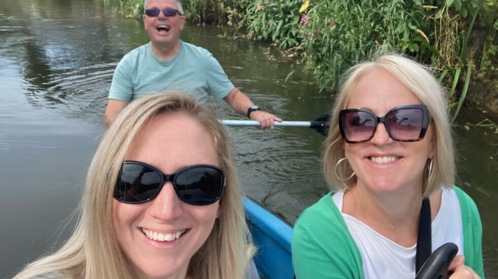 Three Southdown colleagues are rowing on a boat in a river. All three are looking at the camera smiling.