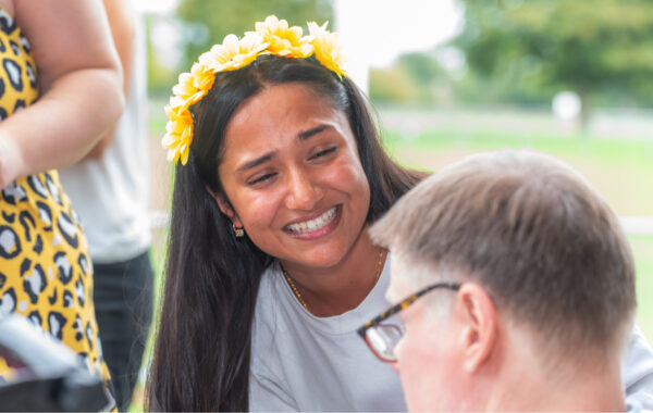 Southdown Support Worker is smiling whilst looking at a client outside. They are wearing a yellow floral headband.