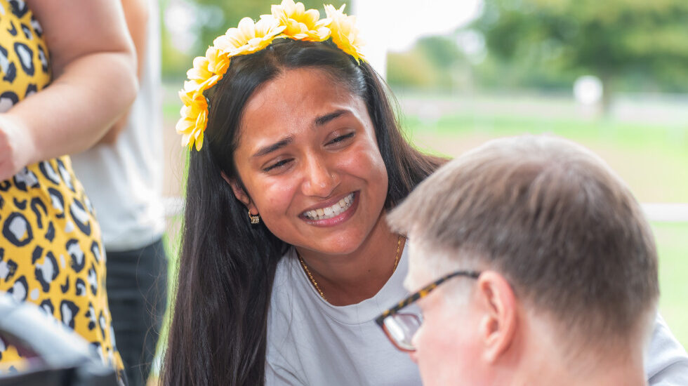 Southdown Support Worker is smiling whilst looking at a client outside. They are wearing a yellow floral headband.