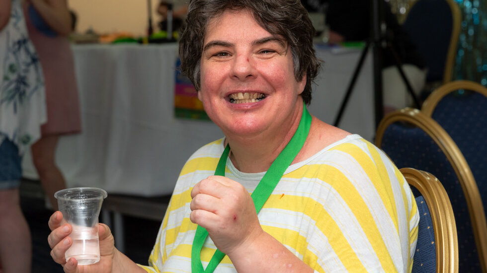 A woman is wearing a stripy yellow t shirt and is smiling whilst looking at the camera.