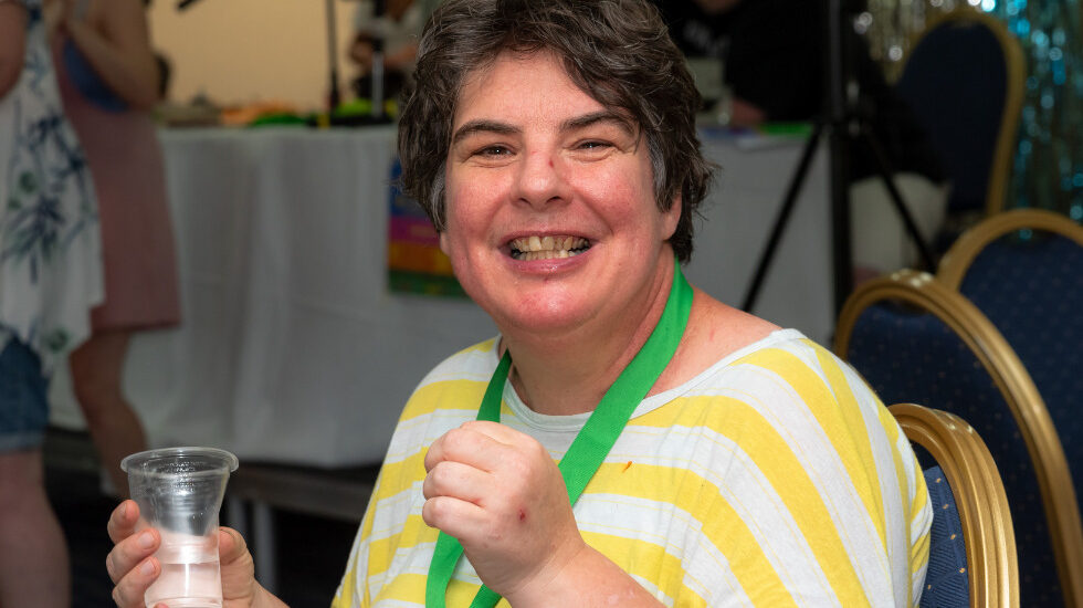A woman is wearing a stripy yellow t shirt and is smiling whilst looking at the camera.