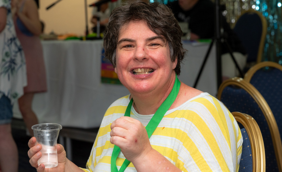 A woman is wearing a stripy yellow t shirt and is smiling whilst looking at the camera.