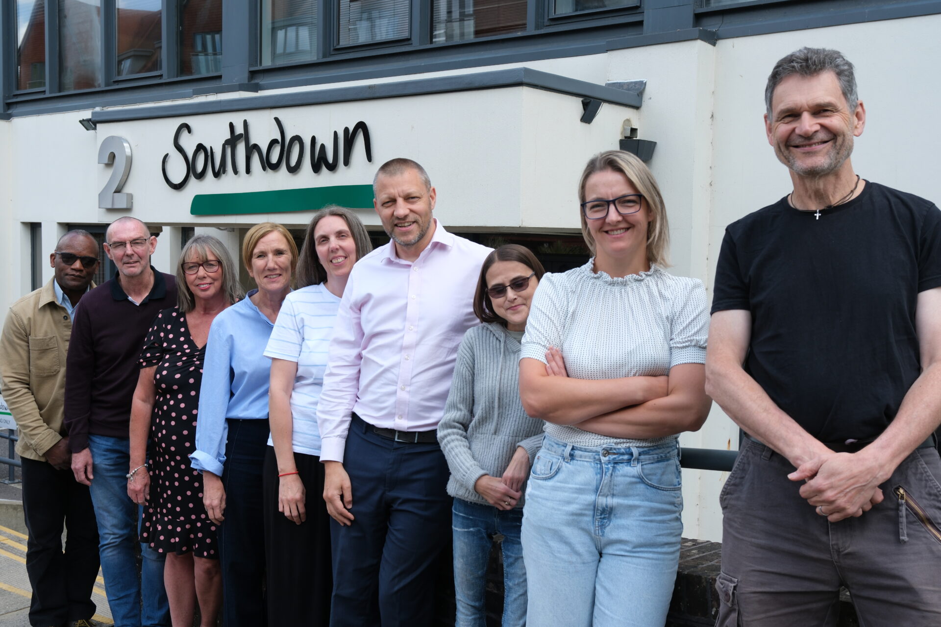 A group of ten Southdown staff members standing in a line outside the Southdown office building. They are smiling and facing the camera. Not all members of the Housing and Central teams are pictured.